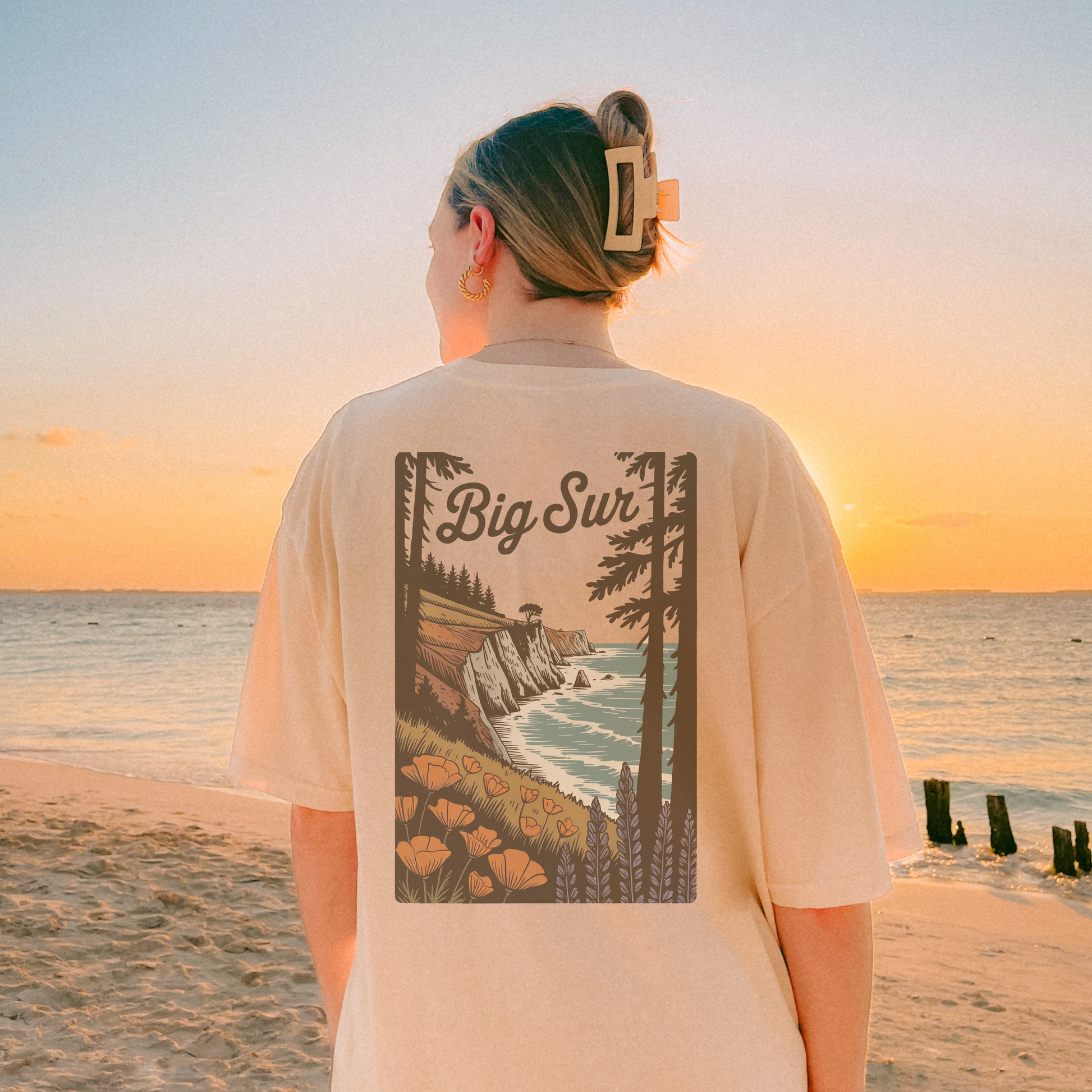 Woman wearing Big Sur State Park shirt with scenic coastal design at sunset on a beach.