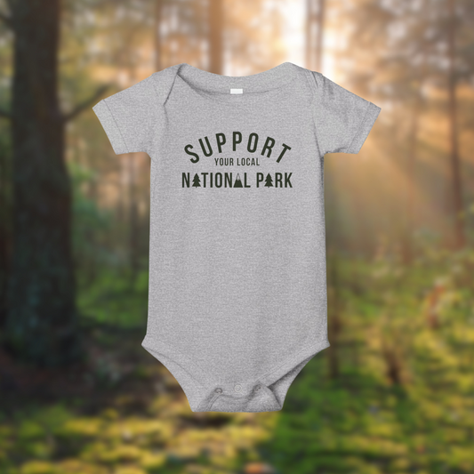 Gray baby onesie with 'Support Your Local National Park' text, set against a forest background, promoting outdoor appreciation.