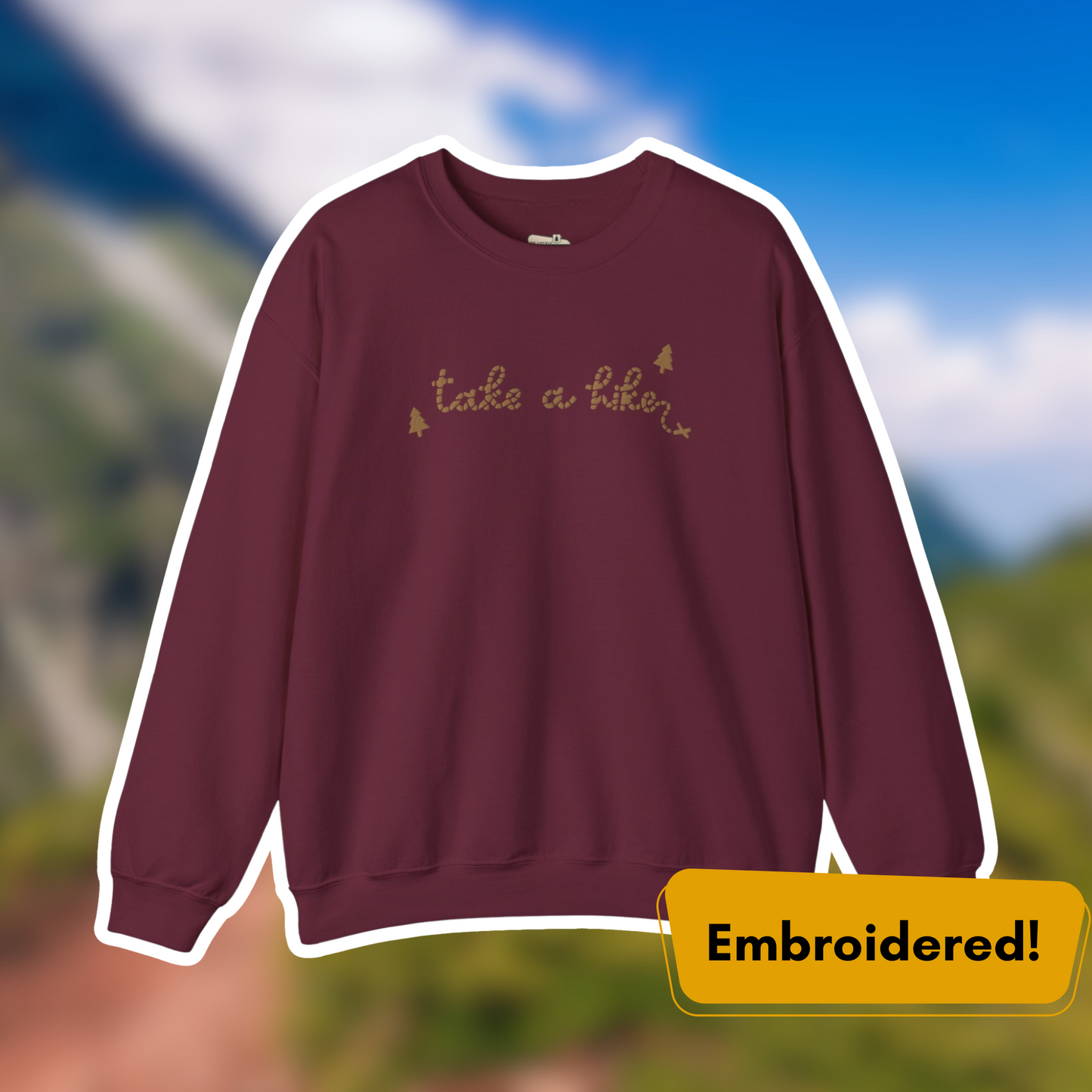 Maroon Take a Hike embroidered crewneck sweatshirt with gold lettering, set against a scenic outdoor background.