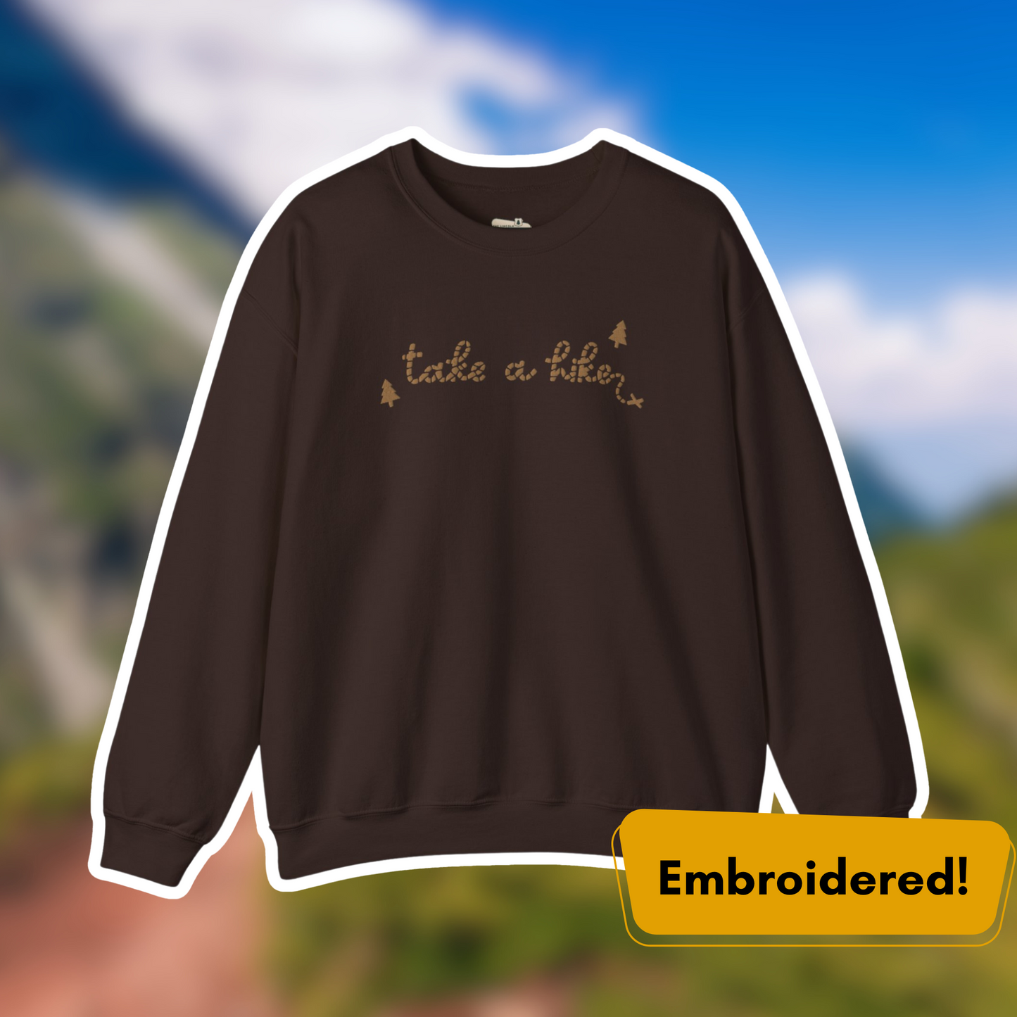 Take a Hike Embroidered Crewneck in brown with gold embroidery against a blurred outdoor background.