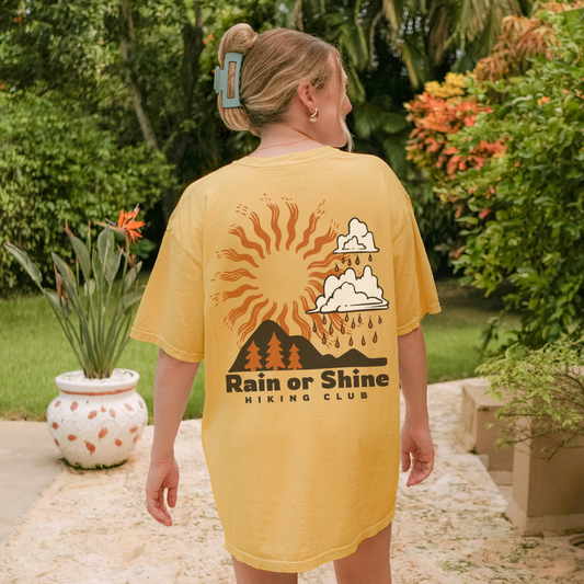 Woman in a yellow unisex tee featuring 'Rain or Shine Hiking Club' design, perfect for outdoor adventures.