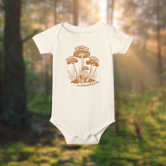 Mushroom Mission baby onesie with explore, cherish, protect design, set in a forest background.