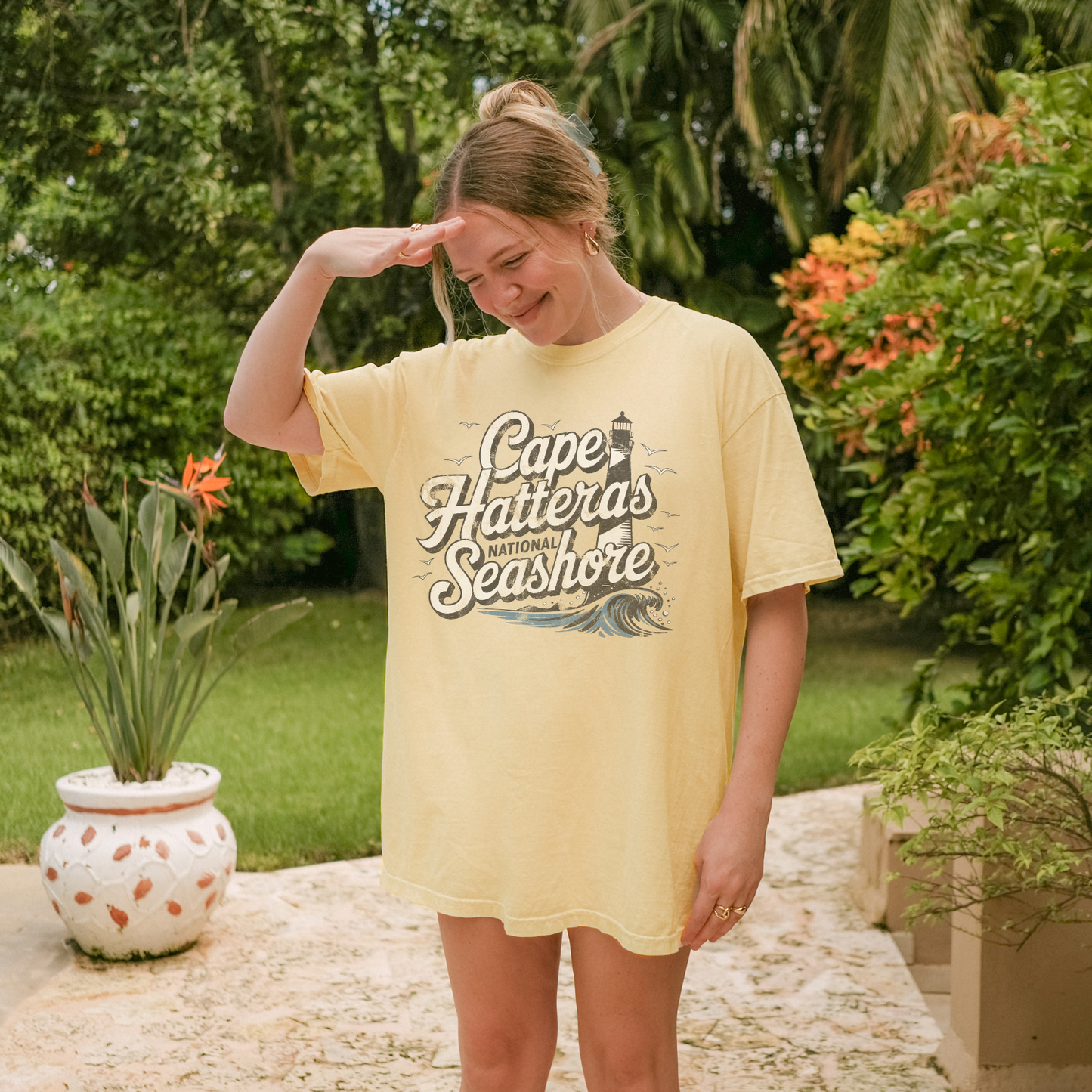 Woman in a yellow Cape Hatteras National Seashore tee shirt, posing outdoors among greenery.