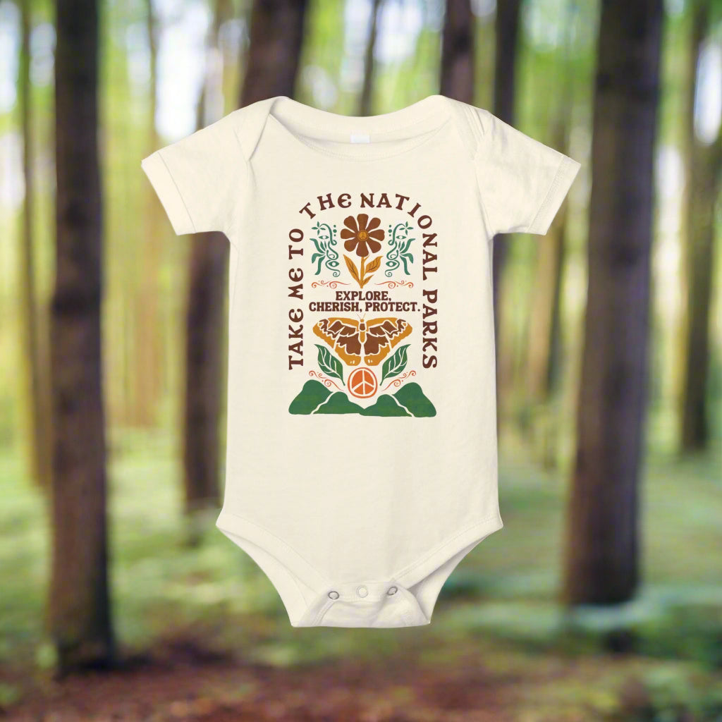 Take Me to the National Parks baby onesie with nature-themed design in a forest setting