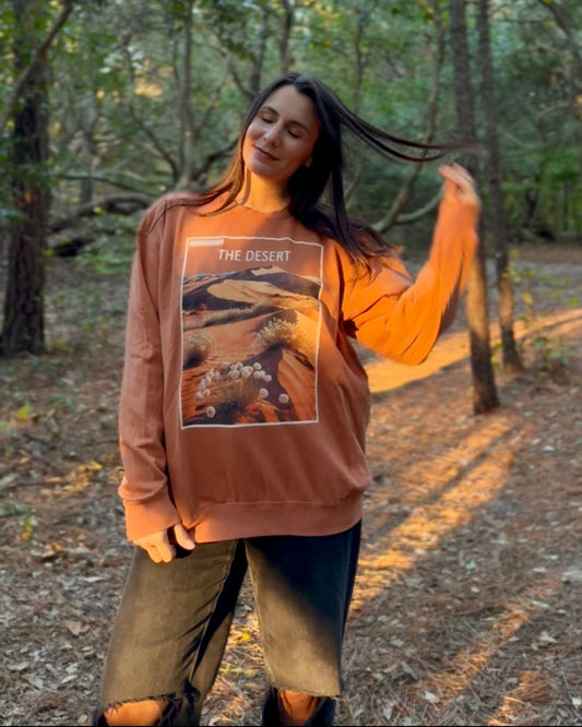 Woman wearing a brown sweatshirt with a graphic design in a forest setting
