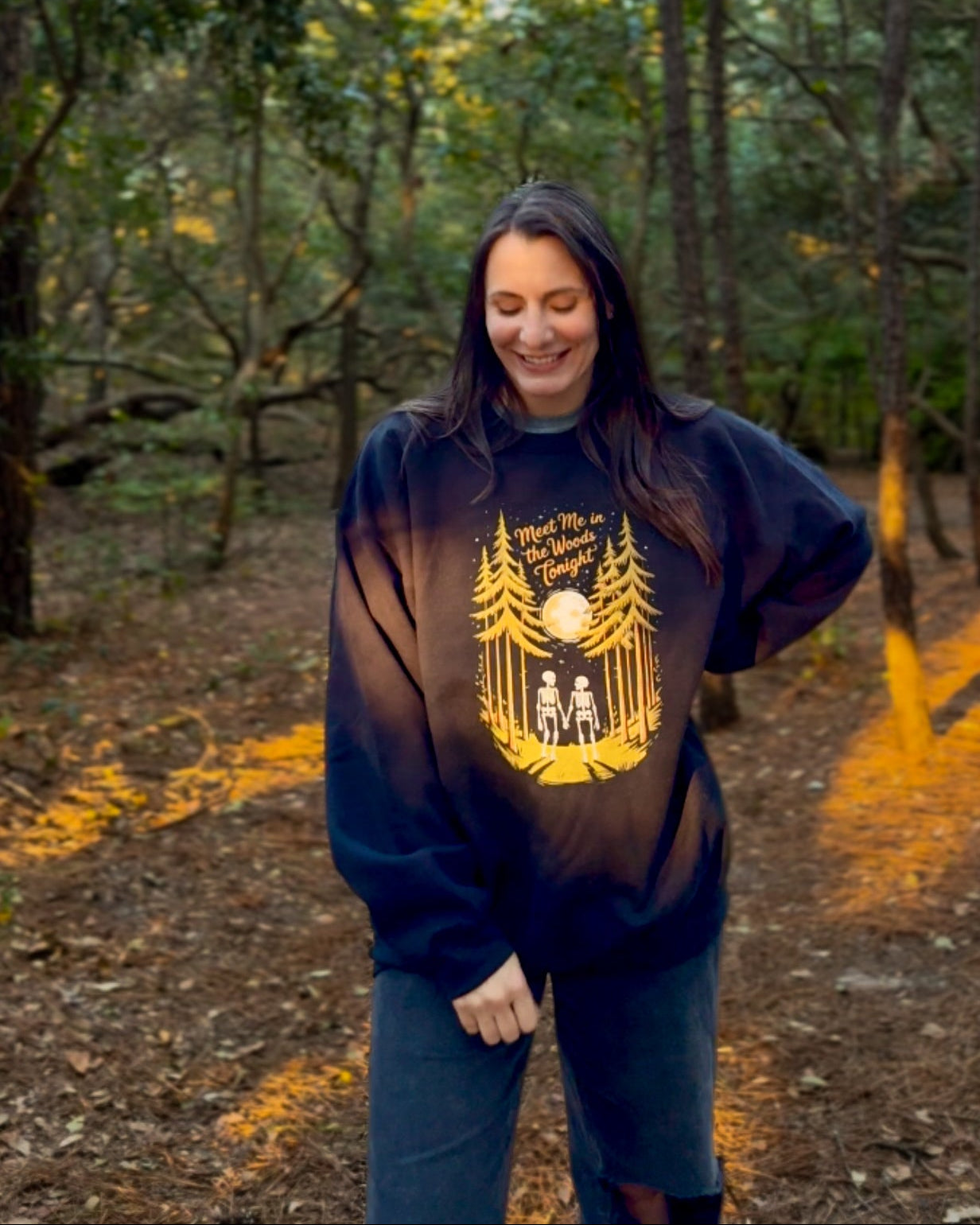 Person wearing a dark hoodie with a yellow graphic in a forest setting