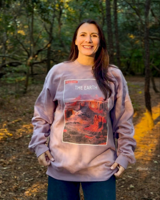 Woman wearing a sweatshirt with an Earth graphic in a forest setting