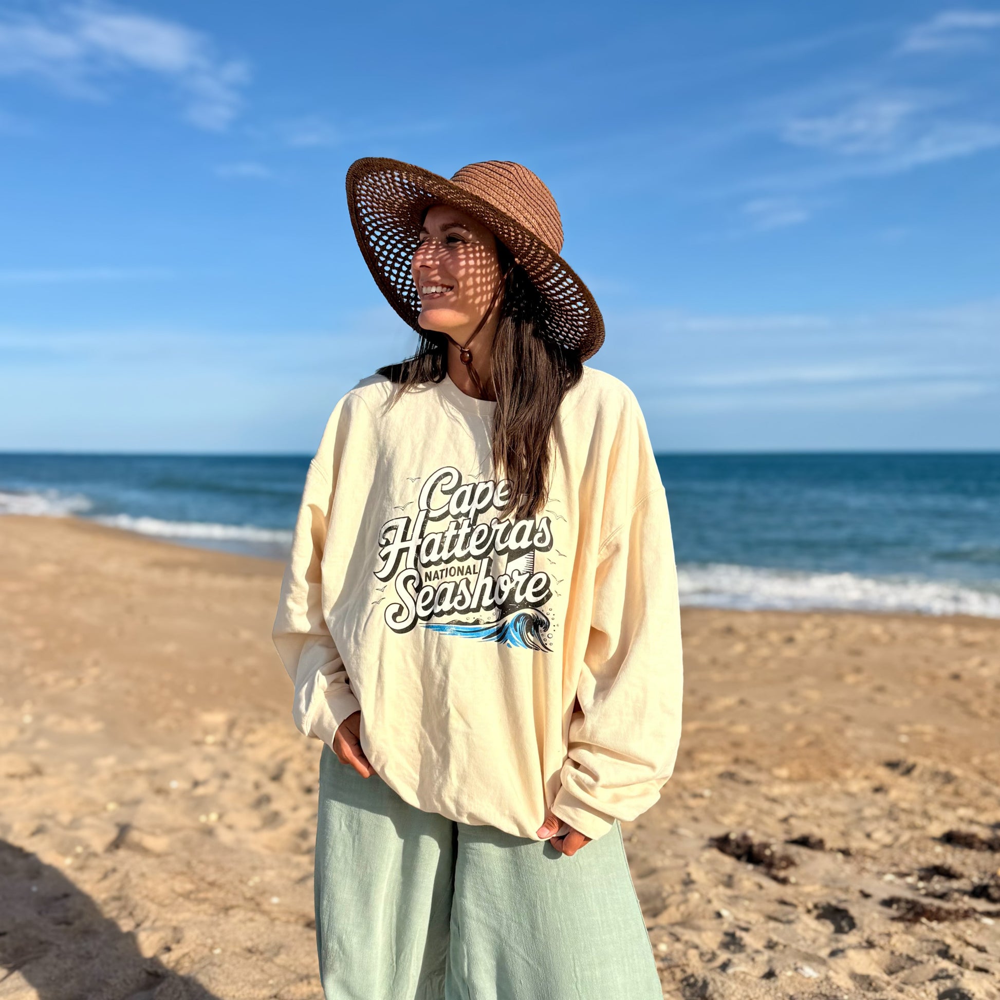Woman wearing Cape Hatteras National Seashore crewneck at the beach with ocean in the background.