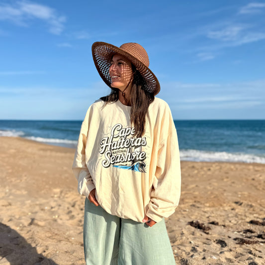 Woman wearing Cape Hatteras National Seashore crewneck at the beach with ocean in the background.