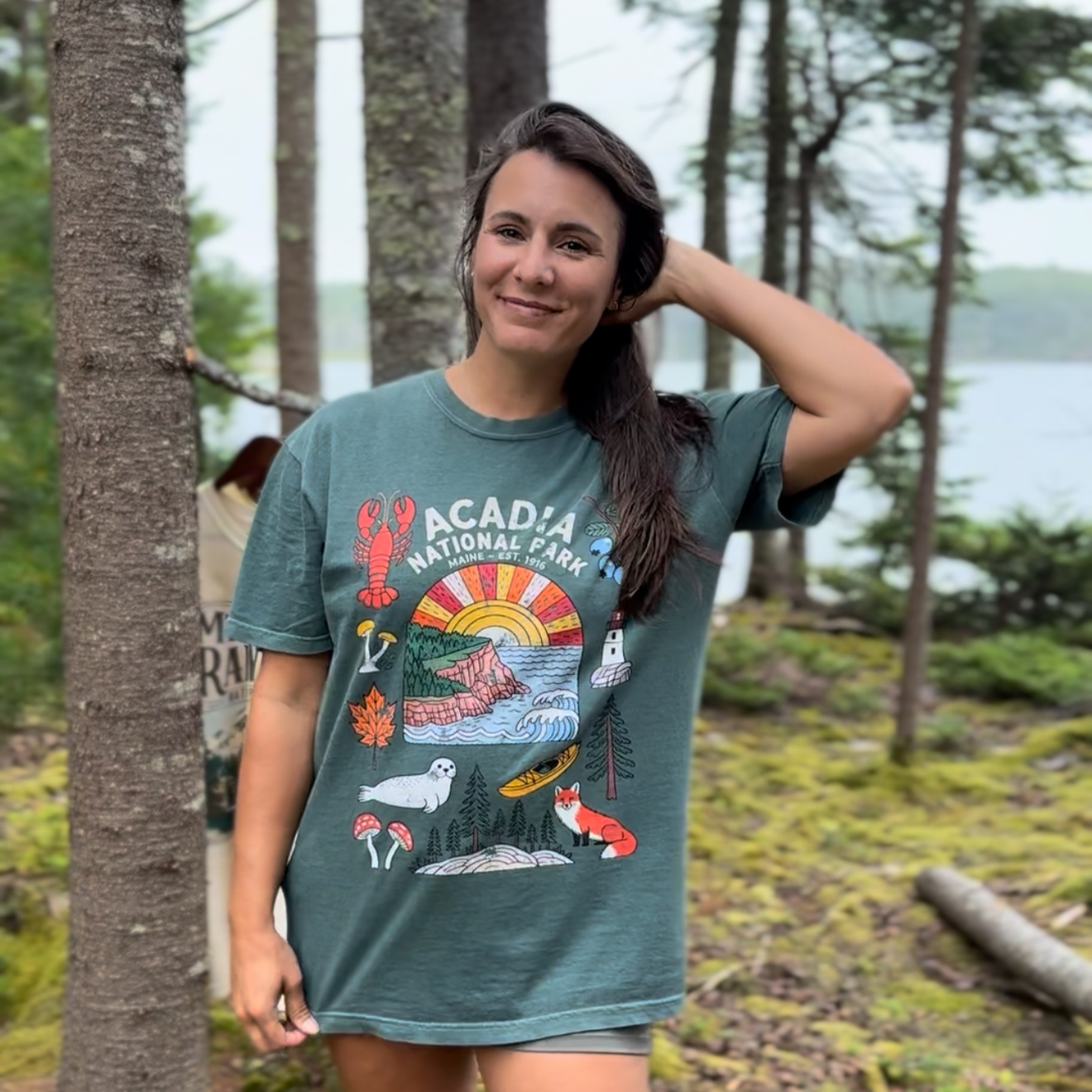 Woman wearing Acadia National Park tee with hand-drawn wildlife illustrations, surrounded by nature.