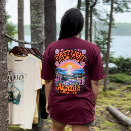 First Light Acadia National Park shirt with vibrant sunrise design in a forest setting.