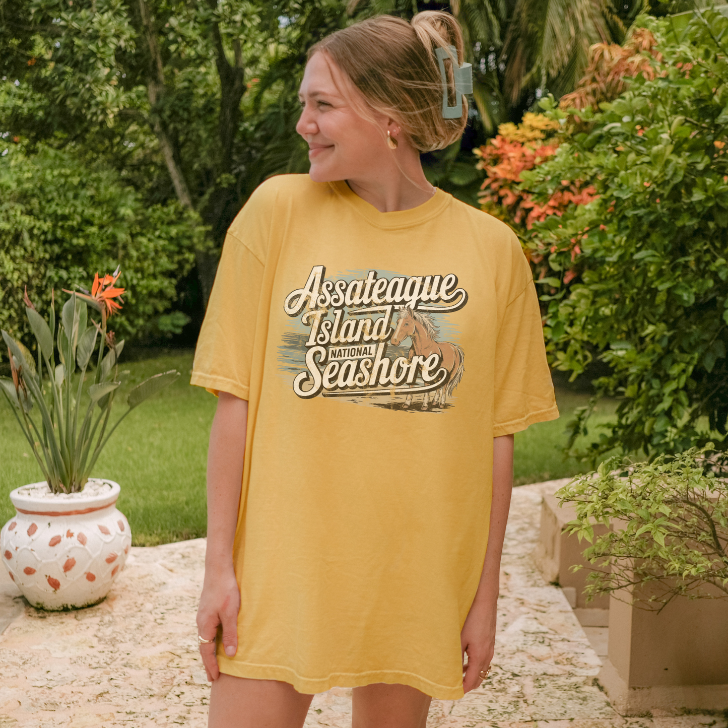 Model wearing a soft yellow Assateague Island National Seashore tee in a coastal garden setting.