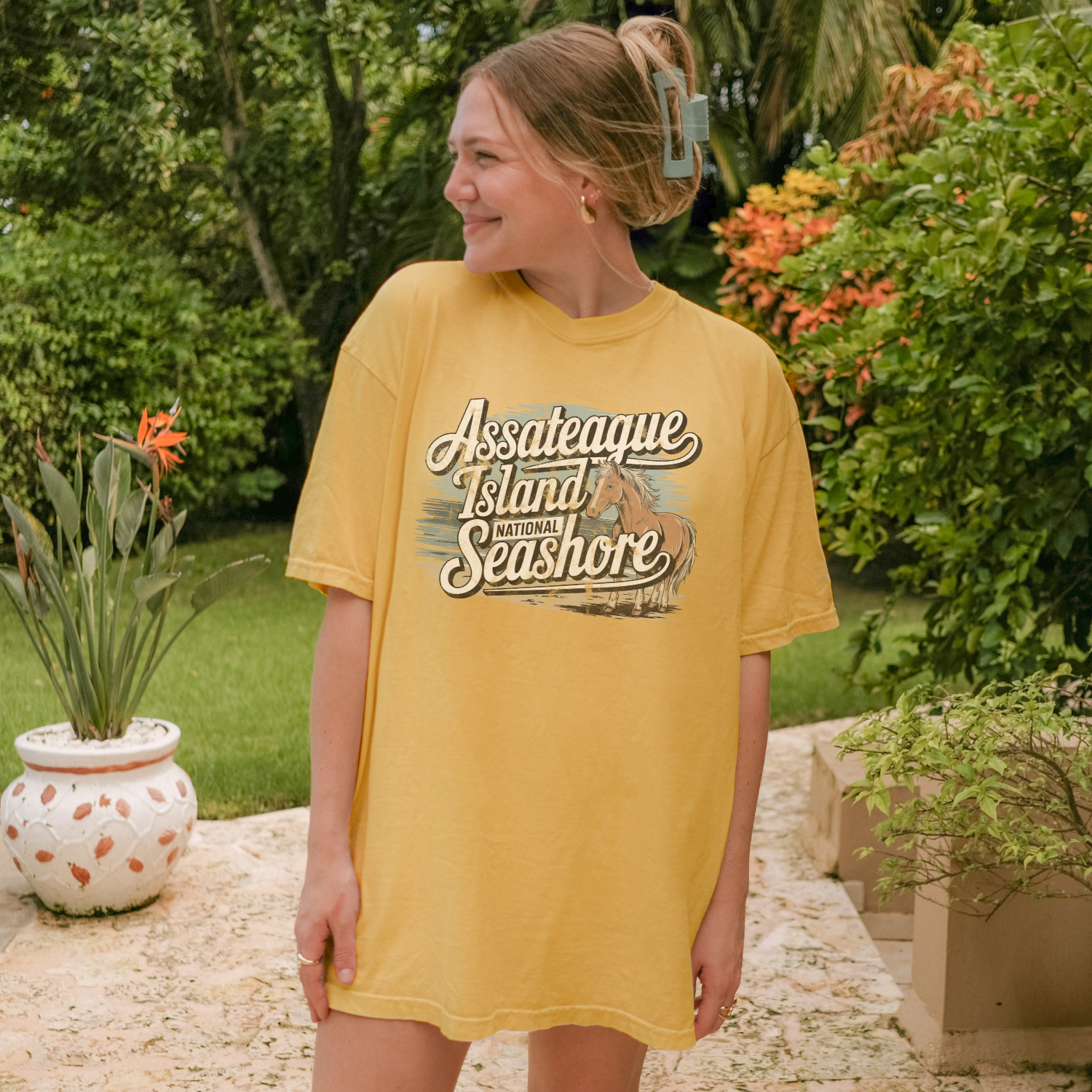 Model wearing a soft yellow Assateague Island National Seashore tee in a coastal garden setting.