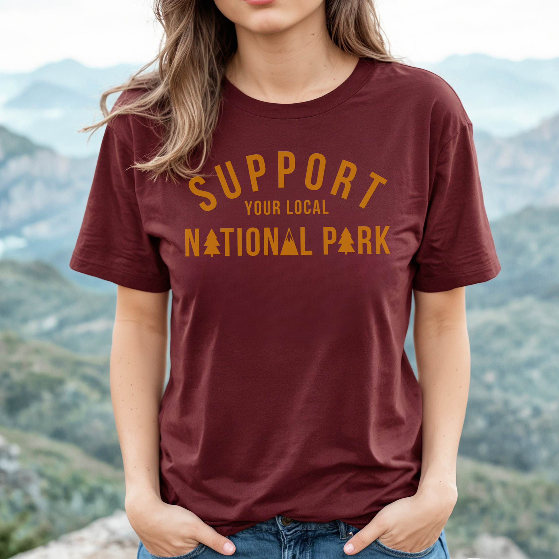 Support Your Local National Park tee in maroon worn by woman against scenic mountains, perfect for outdoor enthusiasts.
