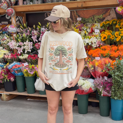 Woman wearing a Redwood National Parks tee in front of colorful flower display.