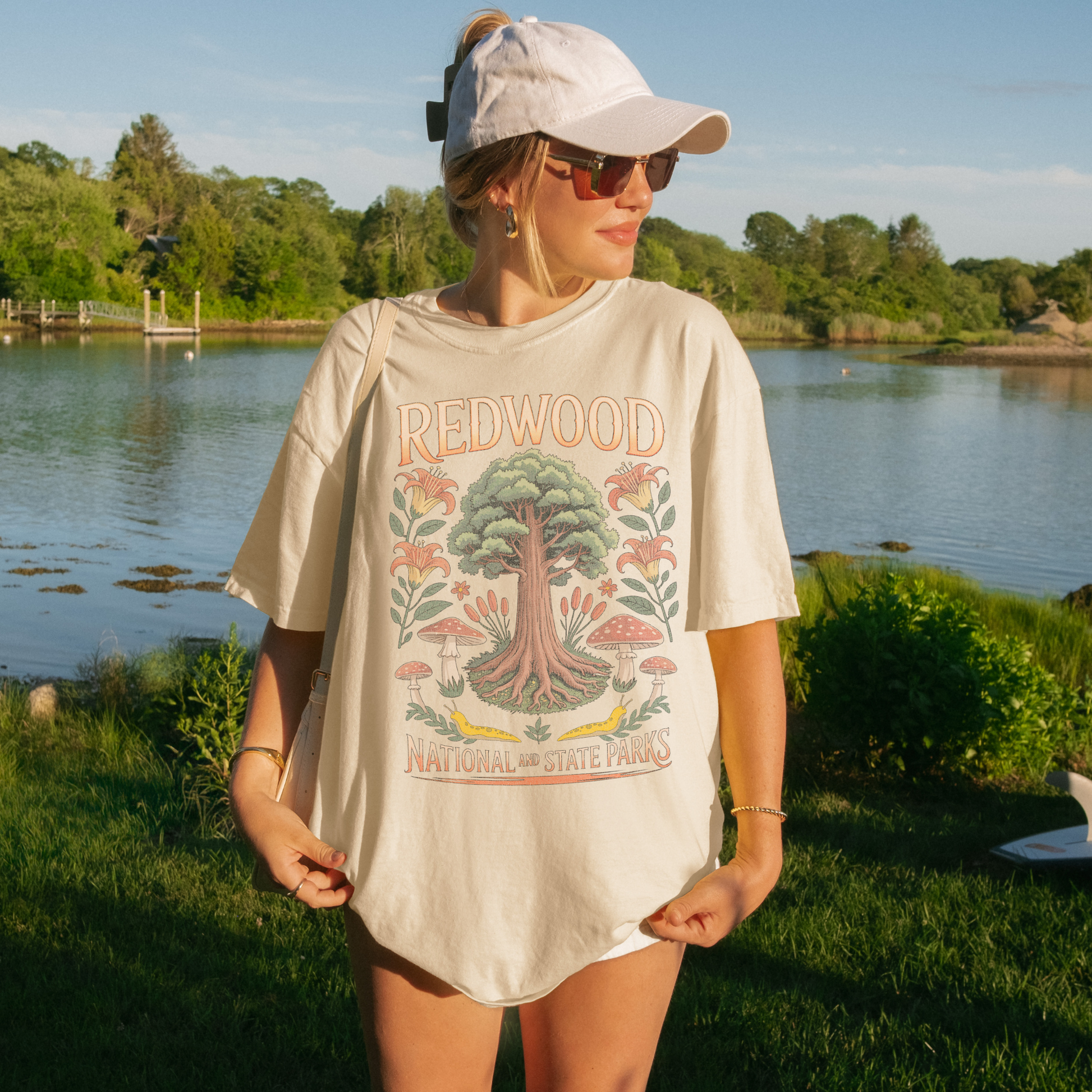 Woman wearing a Redwood National Parks tee by a serene body of water, showcasing nature-inspired design.