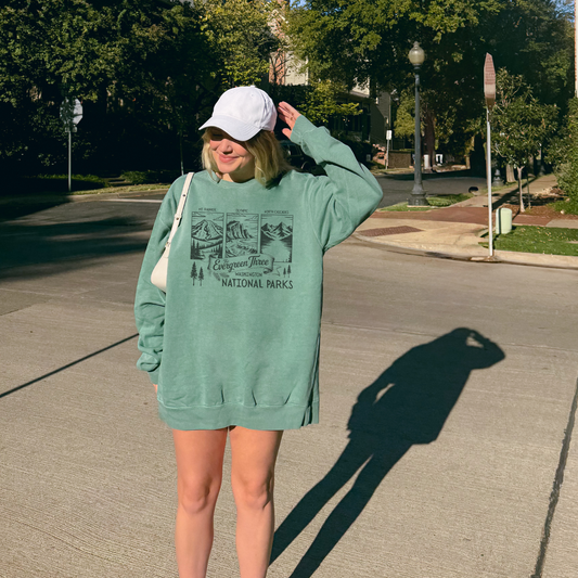 Model wearing a Washington Evergreen Three National Parks sweatshirt on a sunny street.