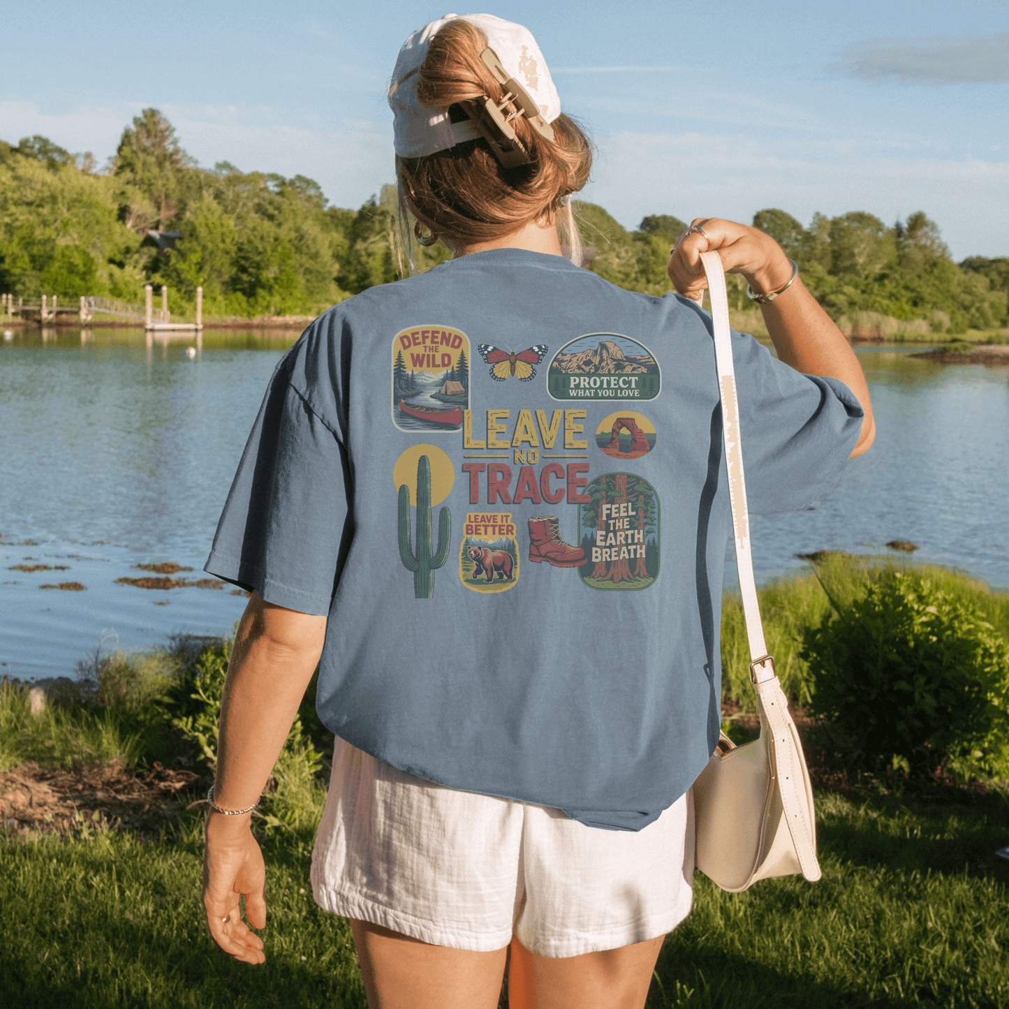 Woman wearing a Leave No Trace tee with vintage patches by a river, promoting outdoor stewardship and adventure.
