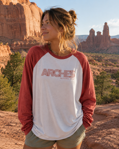 Woman wearing the Arches Heritage Raglan Tee in a scenic desert landscape with red rock formations.