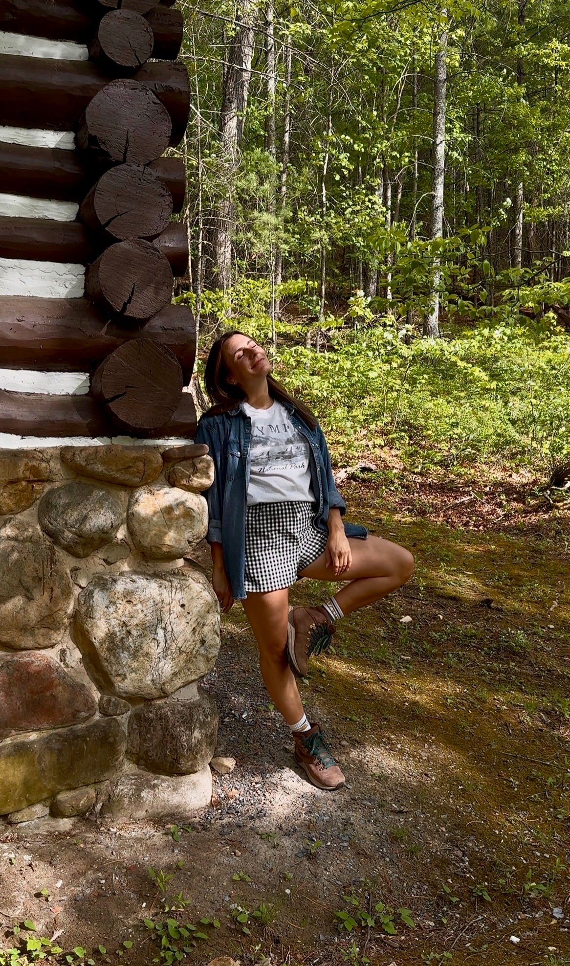 Woman enjoying nature while wearing an Olympic National Park orca tee by a rustic cabin in the woods.