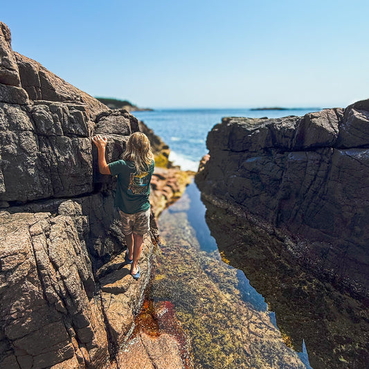 Child exploring rocky shore in youth Cuyahoga Valley National Park Tee, celebrating nature and adventure.