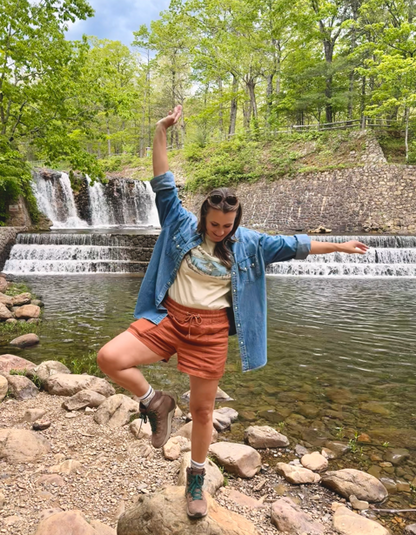 Woman enjoying nature near a waterfall wearing a Crater Lake National Park tee, embodying outdoor adventure.