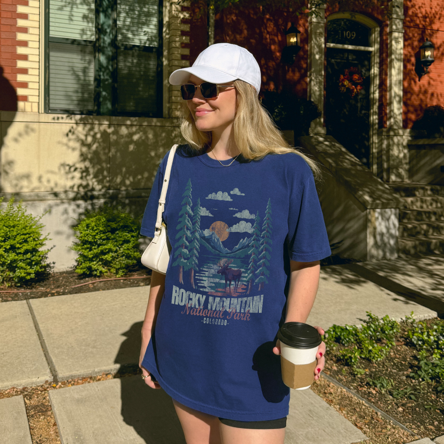 Woman wearing a Rocky Mountain National Park Moose Tee with a mountain landscape design outdoors.