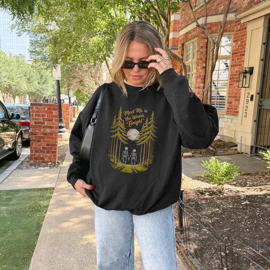 Woman wearing the Meet Me in the Woods sweatshirt with skeletons and trees design in an outdoor setting.